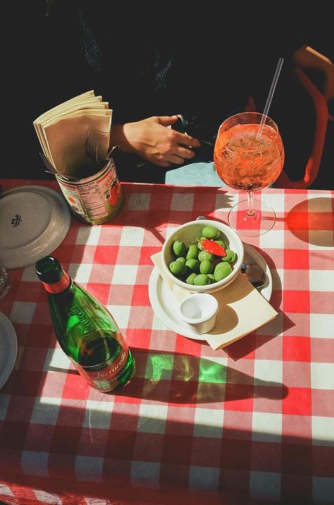 A table set with drinks and a bowl of olives on a red and white checkered tablecloth.