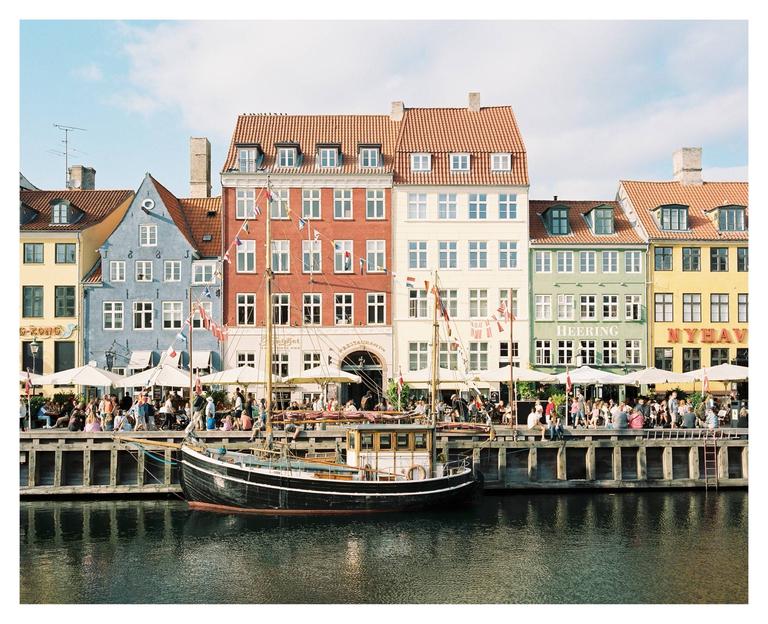 A boat is docked in a canal in front of colorful buildings with people sitting at outdoor cafes.
