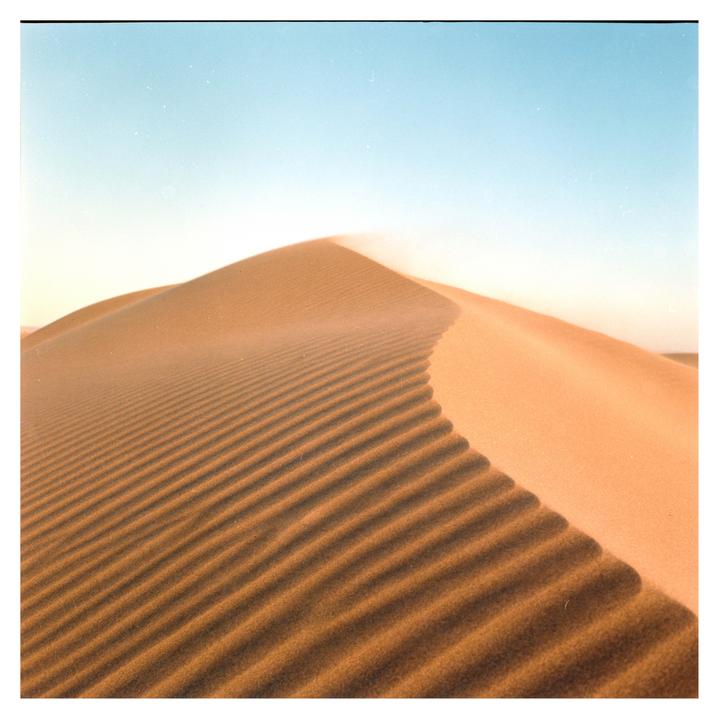 A large sand dune with ripples in the sand is visible under a clear sky.