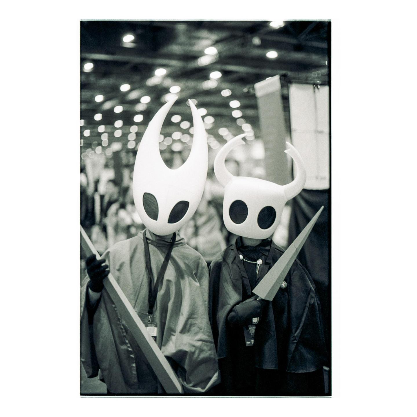 Two people in costumes with large white masks and capes stand side by side.