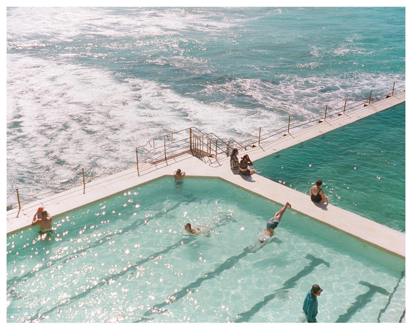 People swim and relax in a concrete pool next to the ocean.