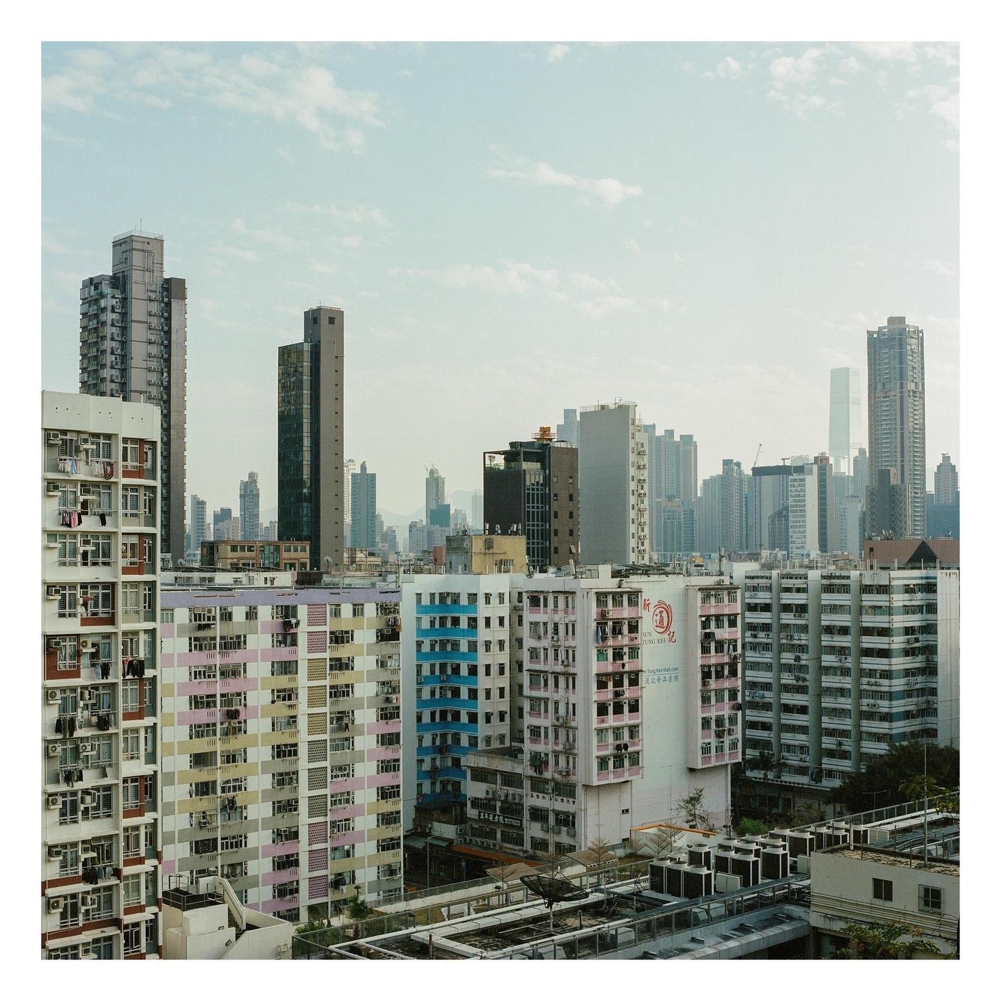 A dense urban landscape features numerous residential and commercial buildings under a cloudy sky.