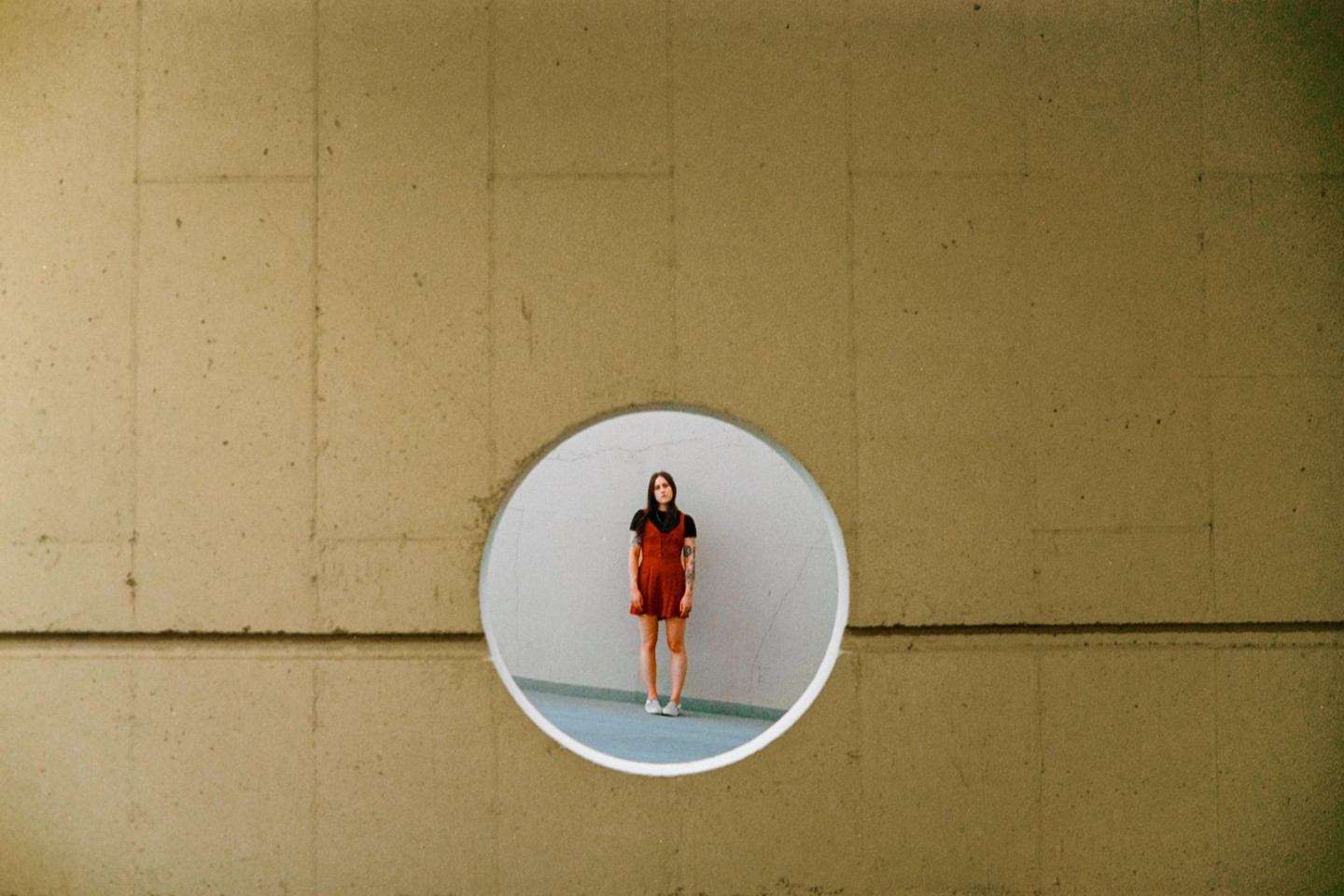 A woman in a red dress stands inside a circular opening in a concrete wall.