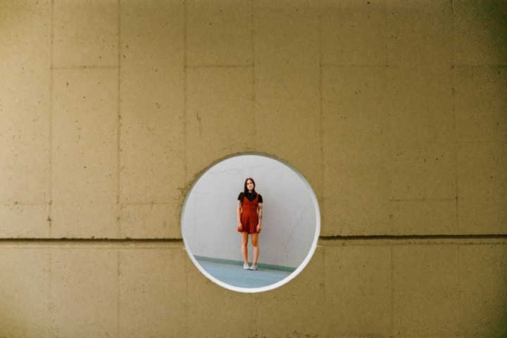 A woman in a red dress stands inside a circular opening in a concrete wall.