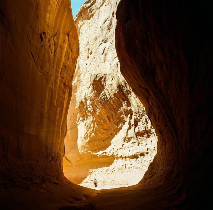 A person stands in a sunlit slot canyon with high rock walls.