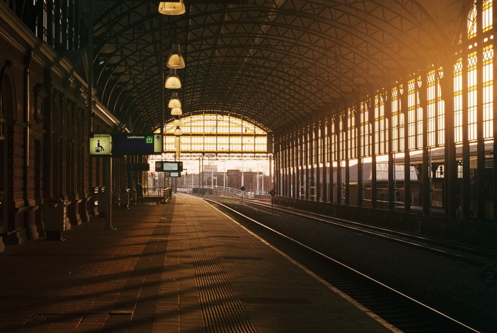 A train station platform is empty with tracks leading into the distance and warm light coming through the windows.