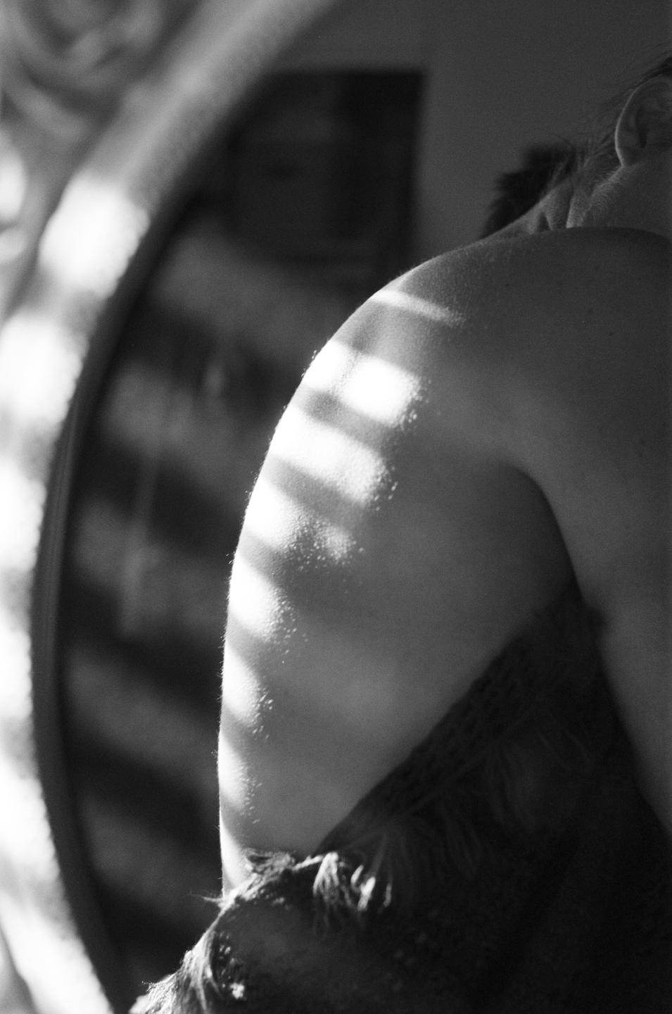 A woman's shoulder is illuminated by striped light in a self-portrait.