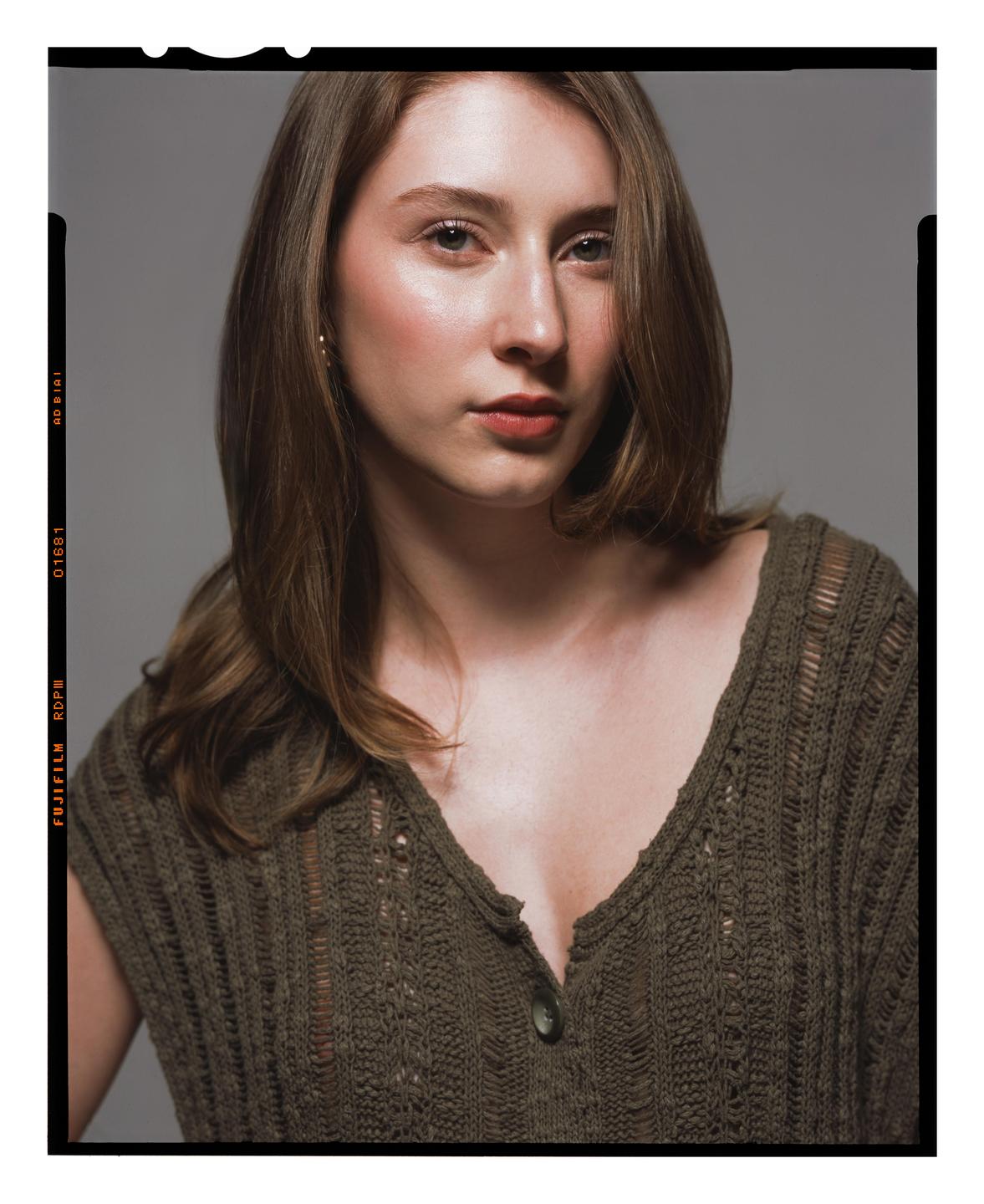 A woman with long hair and a green knitted top looks directly at the viewer.