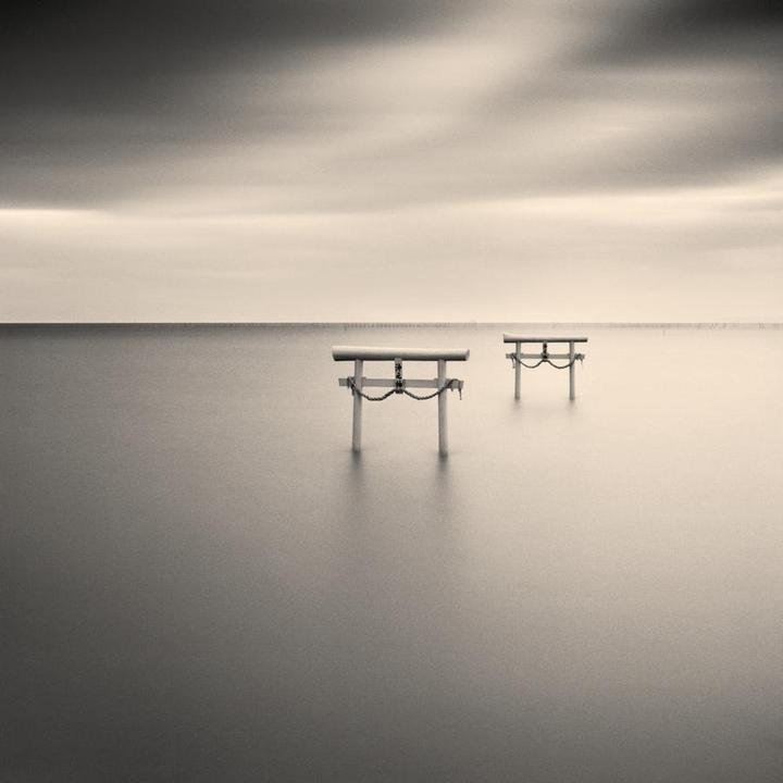 Two torii gates stand in calm water under a cloudy sky.