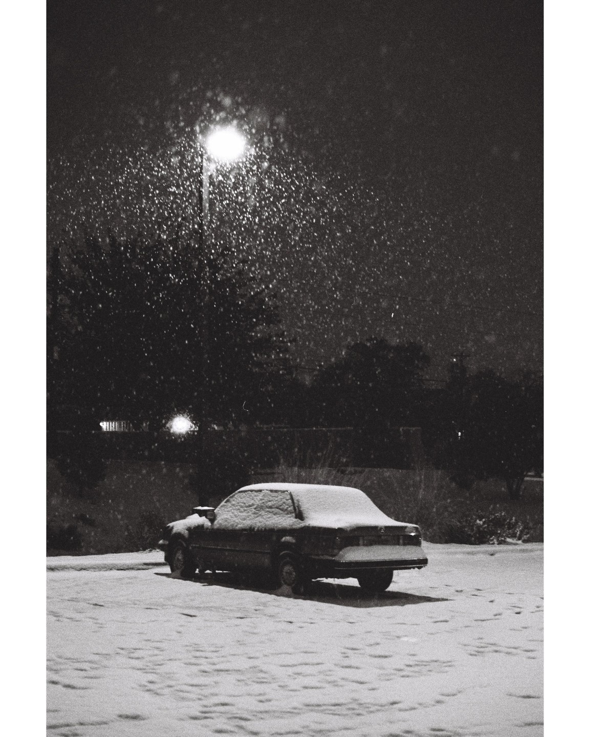 A car is parked in a snowy lot under a street light at night.