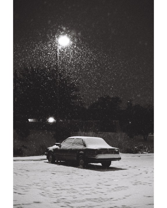 A car is parked in a snowy lot under a street light at night.