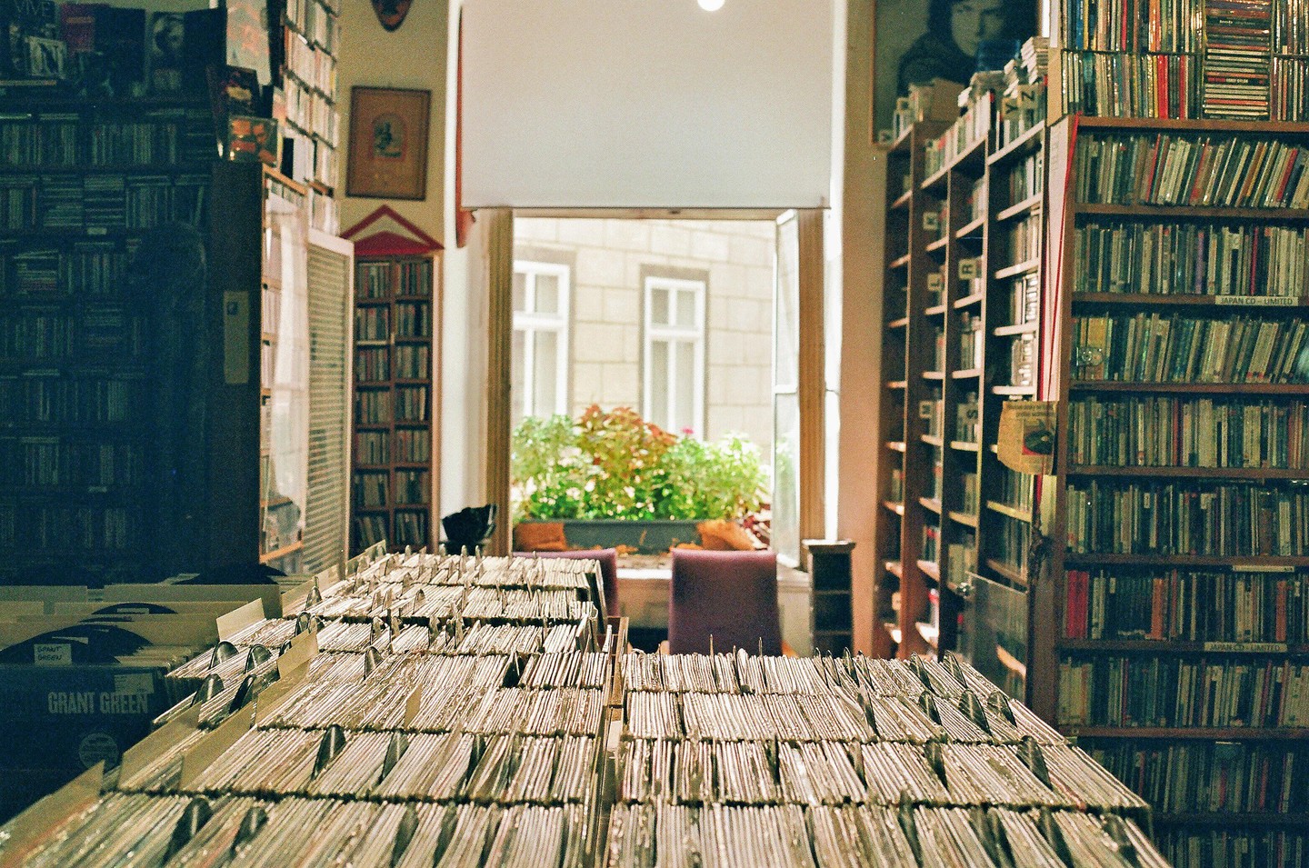 A record shop is filled with records and CDs, with a window looking out onto a courtyard.