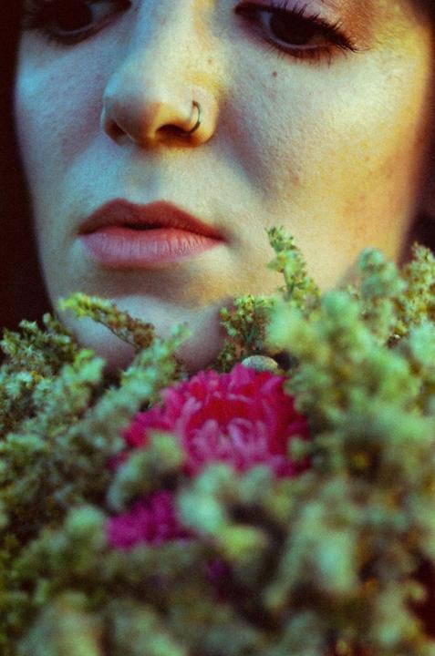 A woman's face with a nose ring is partially obscured by pink and green flowers.
