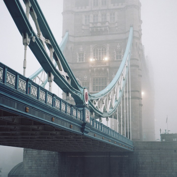 The Tower Bridge is shrouded in fog, with its blue and white structure visible against the hazy background.
