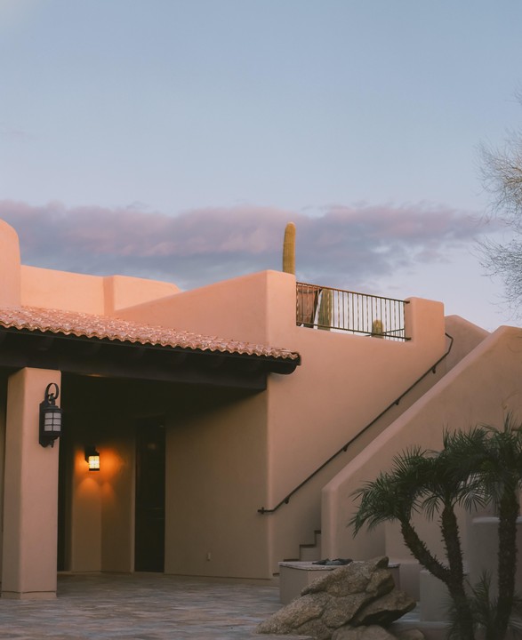 A building with a terracotta roof and a cactus on the upper level is shown under a pastel sky.