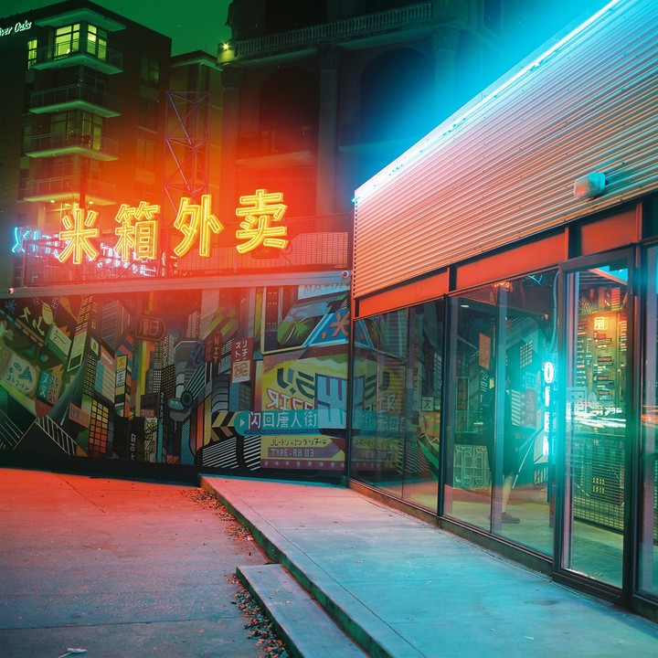 A building with a mural and neon signs is illuminated at night.