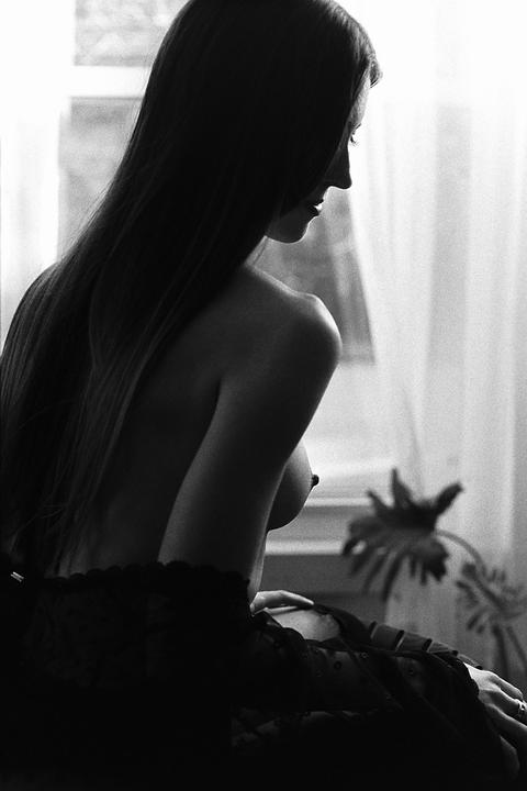 A woman with long hair sits in profile, partially nude, with a plant visible in the background.
