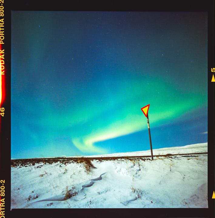 The northern lights glow above a snowy landscape with a triangular road sign.