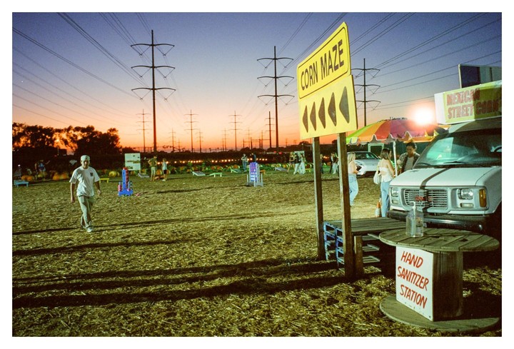 A man walks across a field towards a corn maze sign and a food truck at sunset.