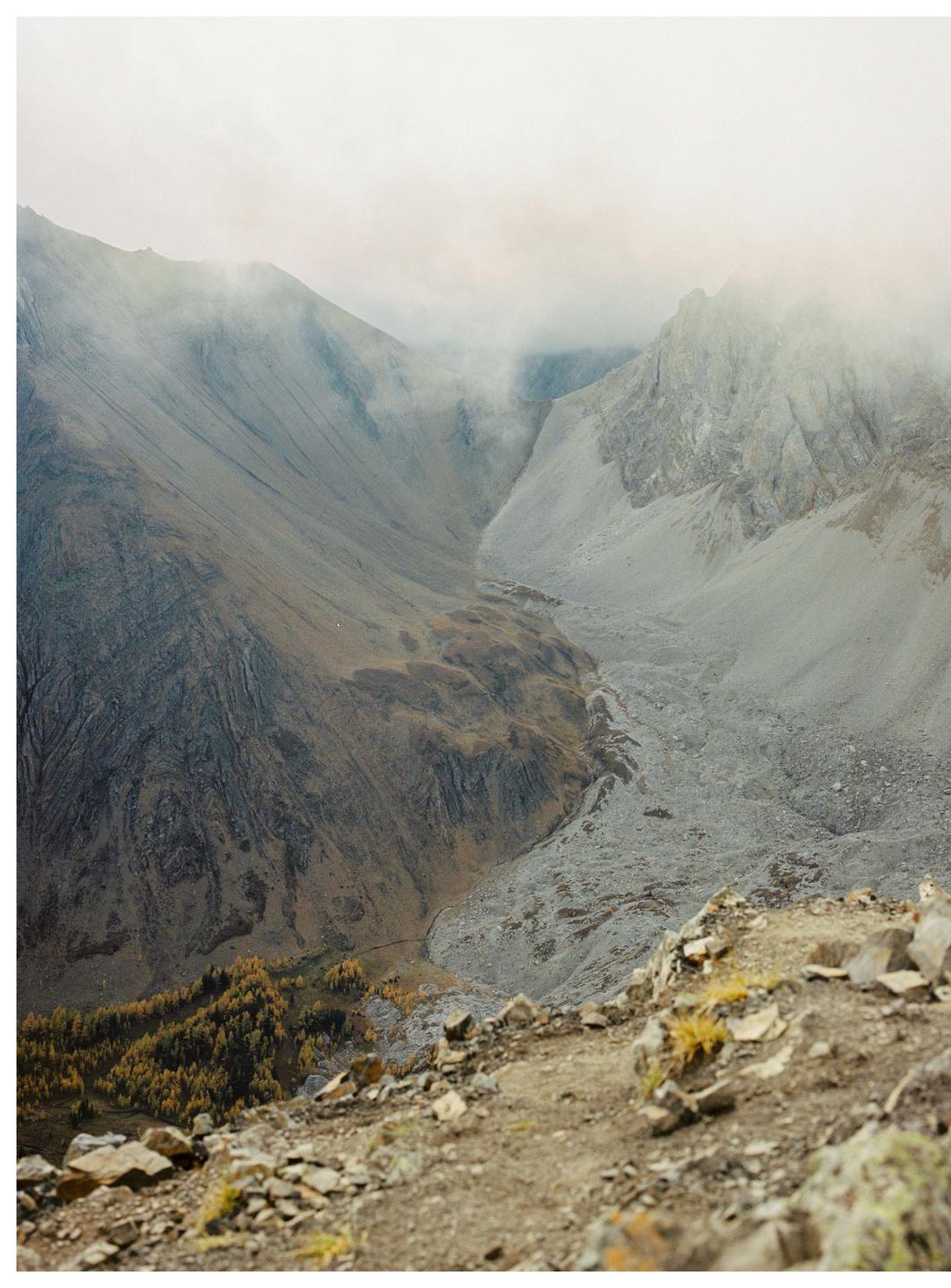 A misty mountain valley with a rocky riverbed and autumn trees is visible from a high vantage point.