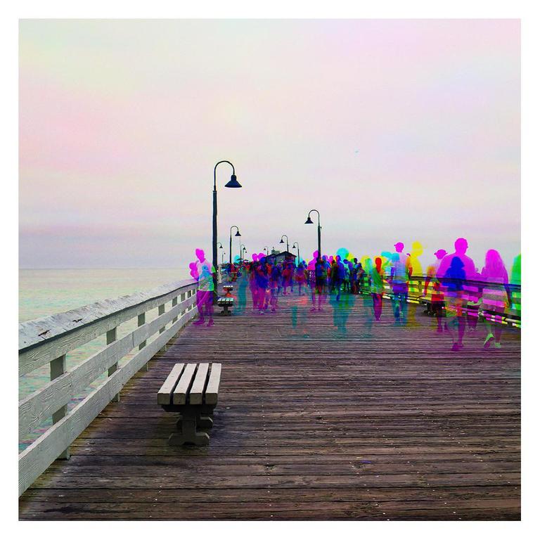 A crowd of people with colorful, ghost-like outlines walks along a wooden pier next to the ocean.