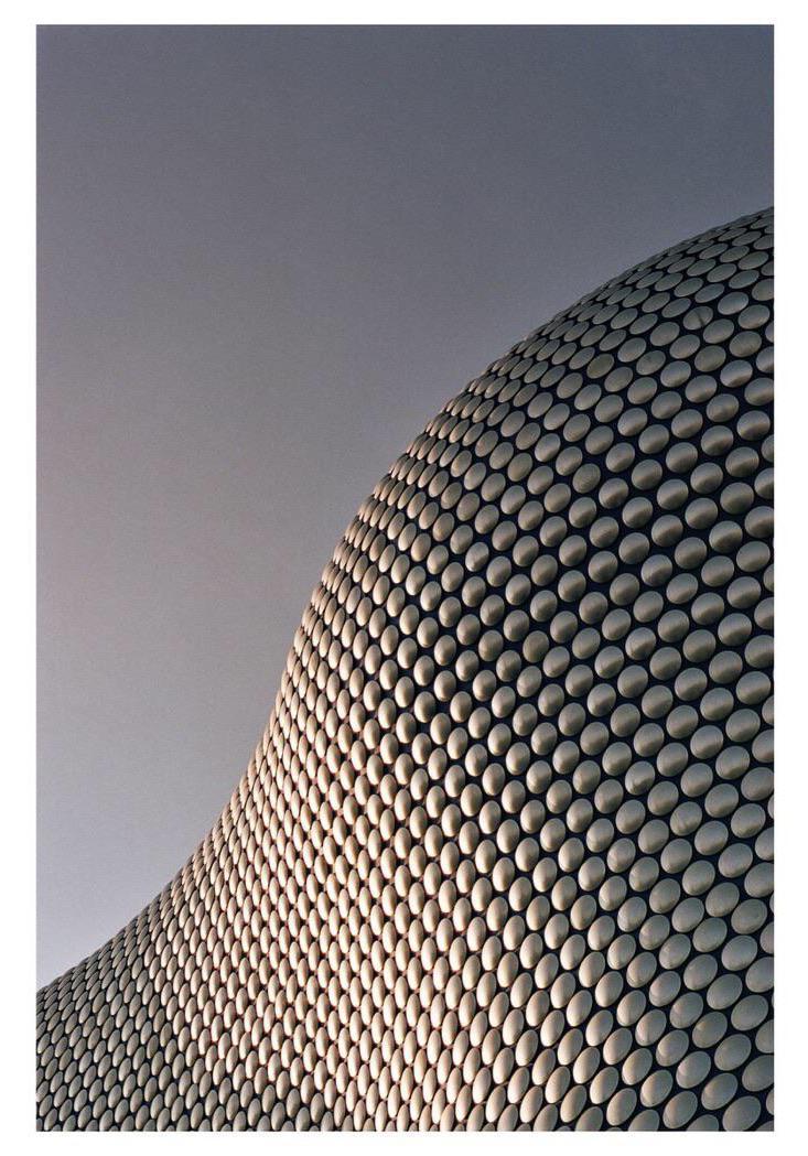 The facade of a modern building covered in metallic discs curves against a gray sky.
