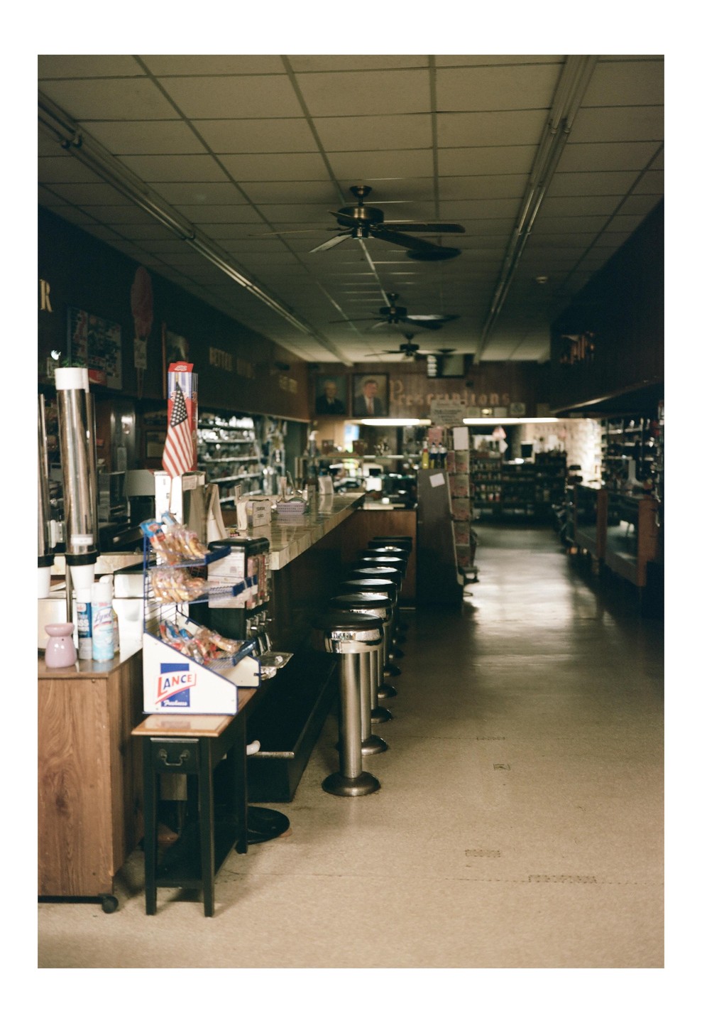 A long counter with stools lines a narrow store with ceiling fans and an American flag.