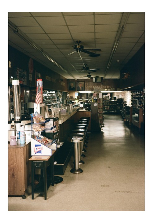A long counter with stools lines a narrow store with ceiling fans and an American flag.