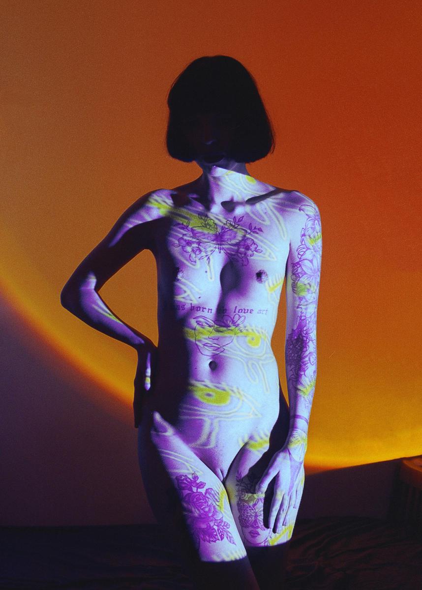 A woman stands with patterns and text projected onto her body against an orange background.