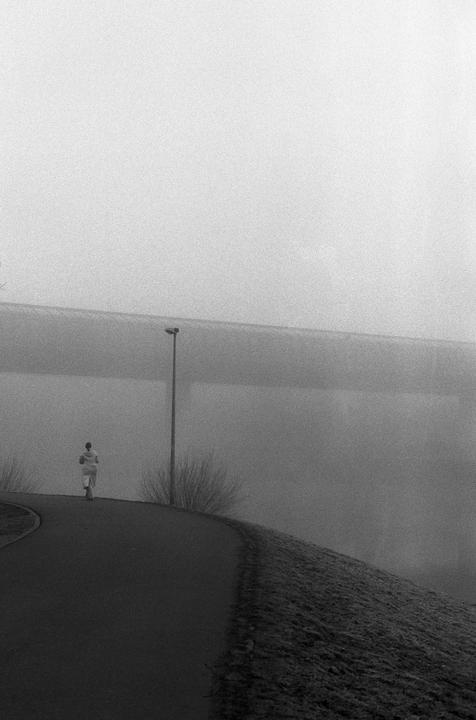 A person walks along a winding road next to a street light in a hazy landscape.