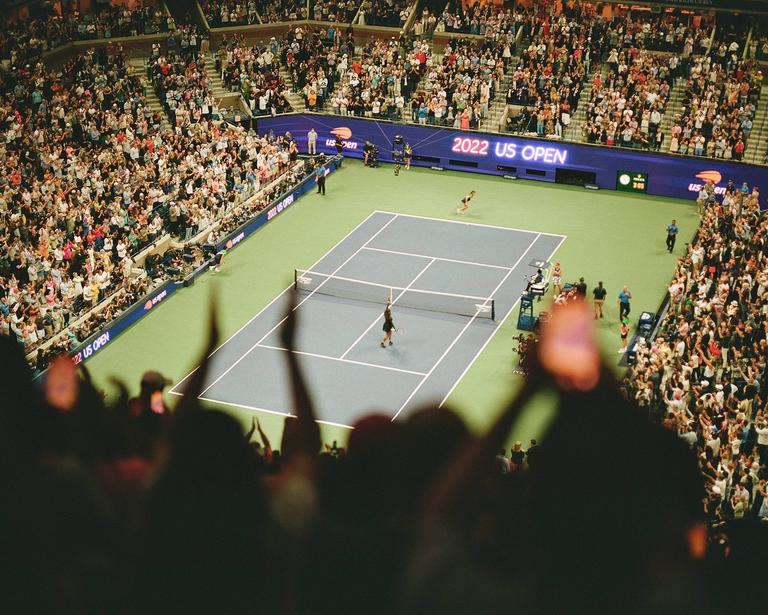 A tennis player serves on a court surrounded by a large crowd in a stadium.