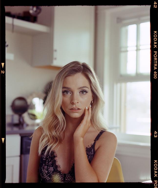 A woman with long blonde hair and a lace top poses for a portrait in a kitchen.