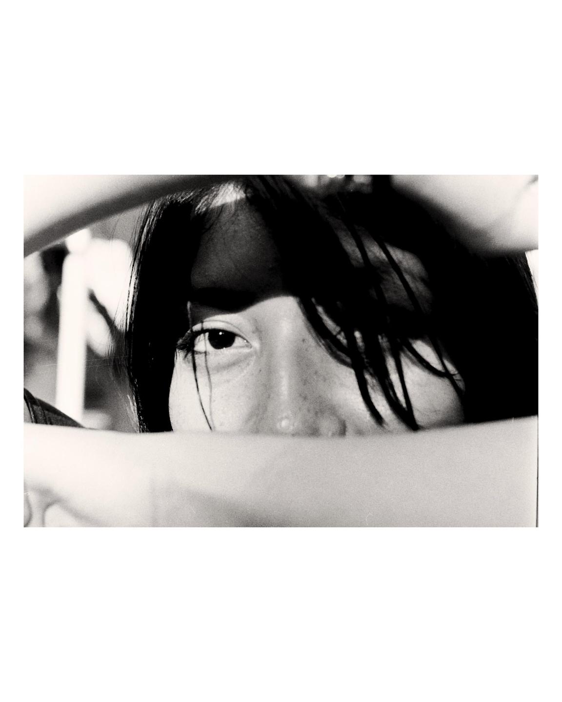 A woman's face is partially obscured by her arm and hair, with one eye looking directly at the viewer.
