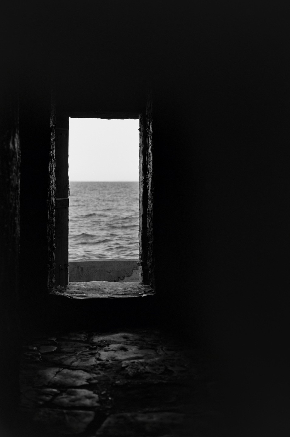 A dark, narrow opening frames a view of the ocean under a bright sky.