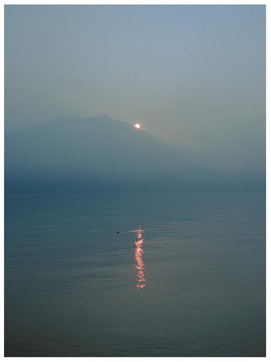A hazy sunset over a lake with a mountain in the background and a small boat in the foreground.