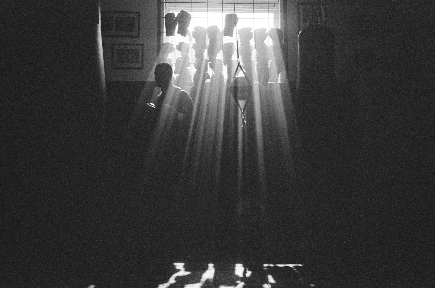 Sunlight streams through a window, illuminating a man and boxing equipment in a dark room.