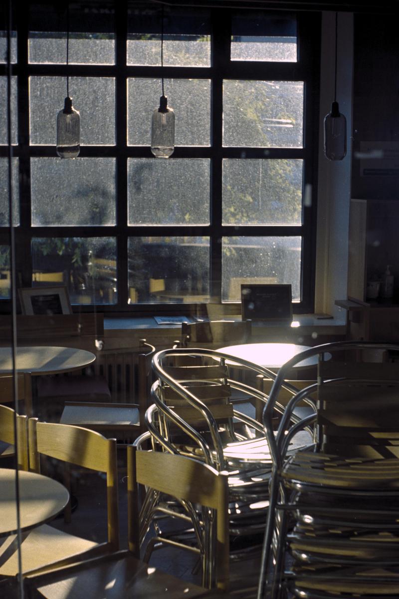 Sunlight streams through a large window into a cafe with stacked chairs and tables.