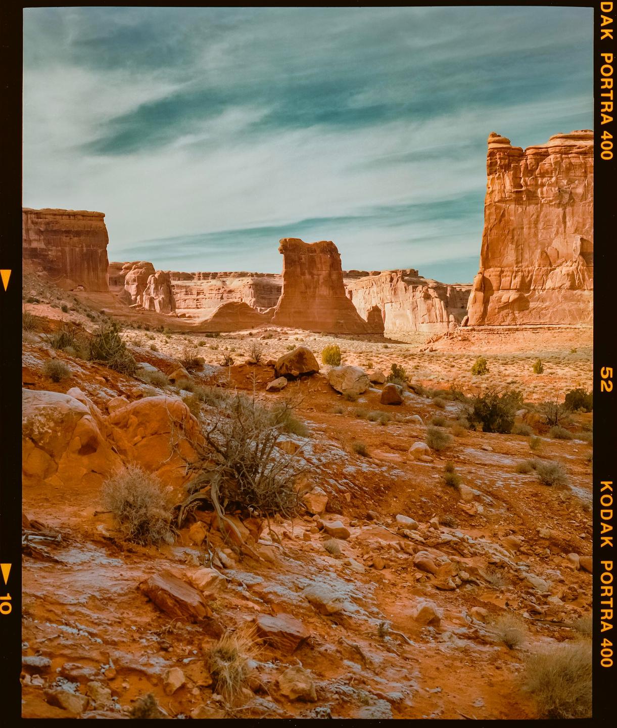 A desert landscape features red rock formations under a blue sky with wispy clouds.