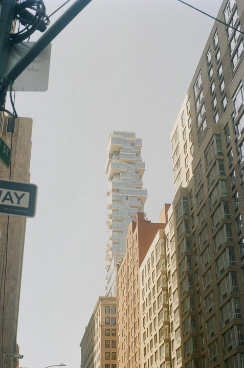 A tall, modern building with many balconies rises above other buildings and a street sign.