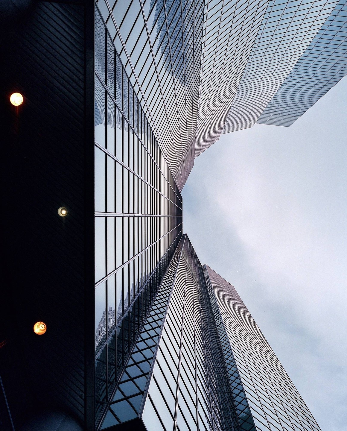 A low-angle view shows the glass facade of a skyscraper reflecting the sky and another building.