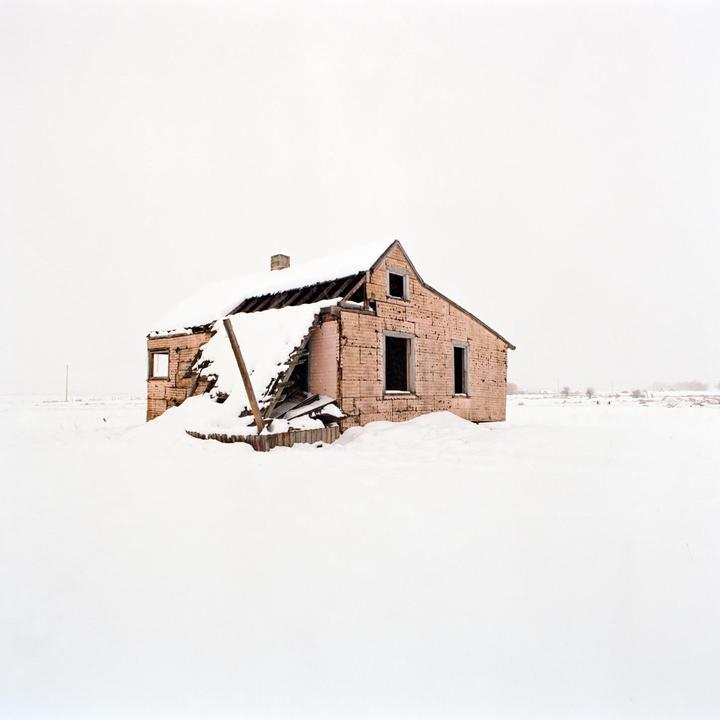 An abandoned house with a partially collapsed roof is covered in snow.
