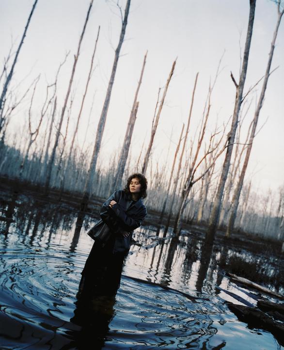 A woman stands in a body of water surrounded by bare trees.