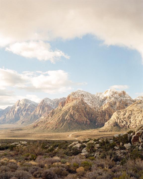 A vast desert landscape features snow-capped mountains under a partly cloudy sky.