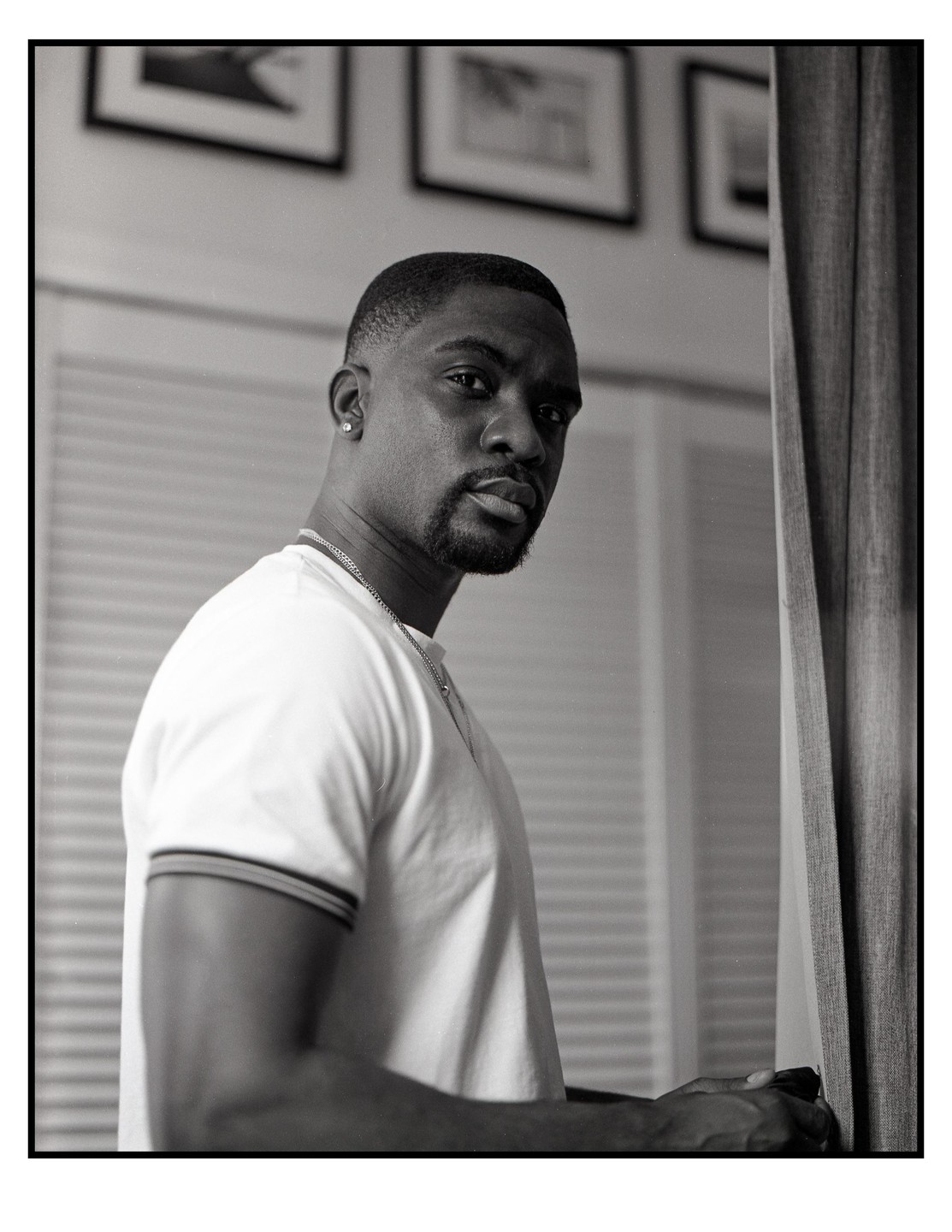 A man with a beard and a white t-shirt looks over his shoulder at the viewer.