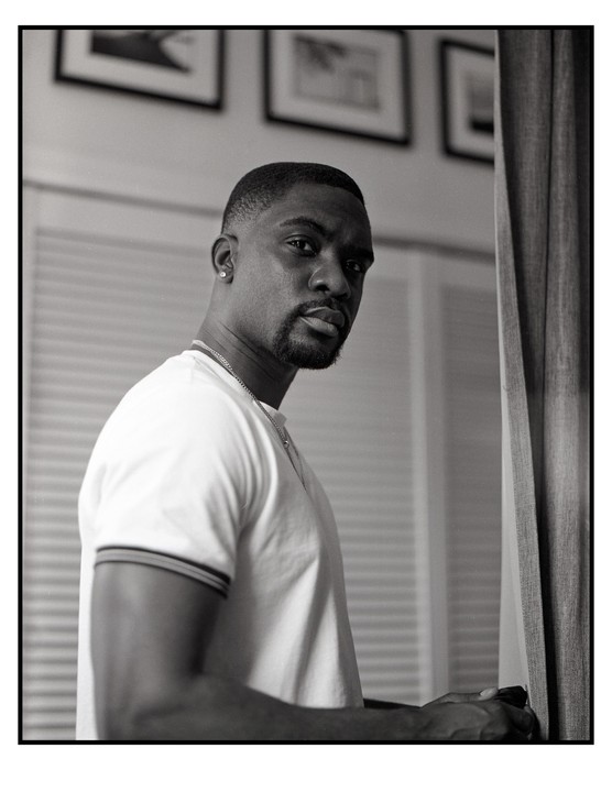 A man with a beard and a white t-shirt looks over his shoulder at the viewer.