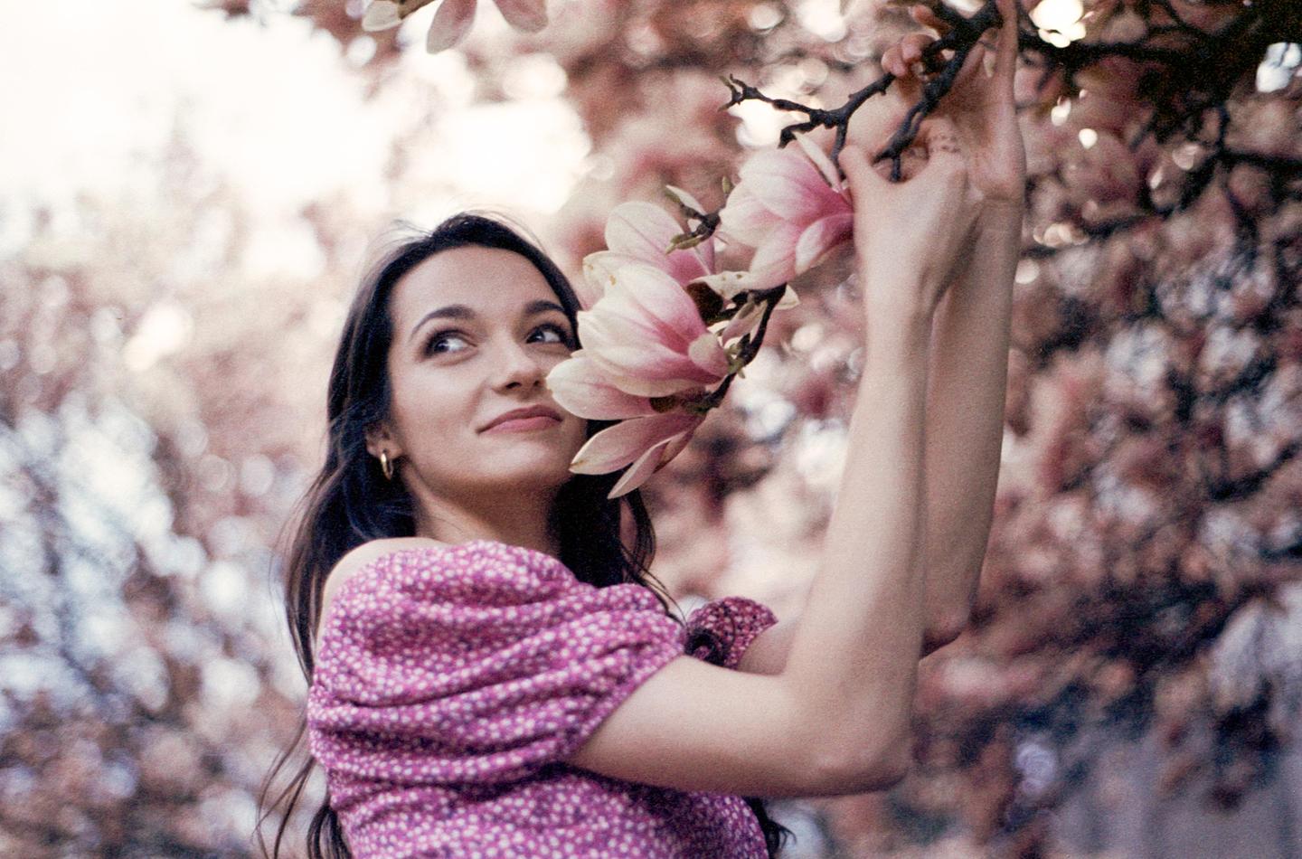 A woman in a pink top looks up at a magnolia branch she is holding.