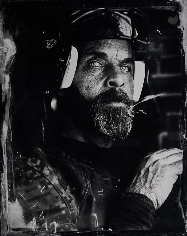 A man with a beard and headphones looks up, with smoke coming from his mouth.