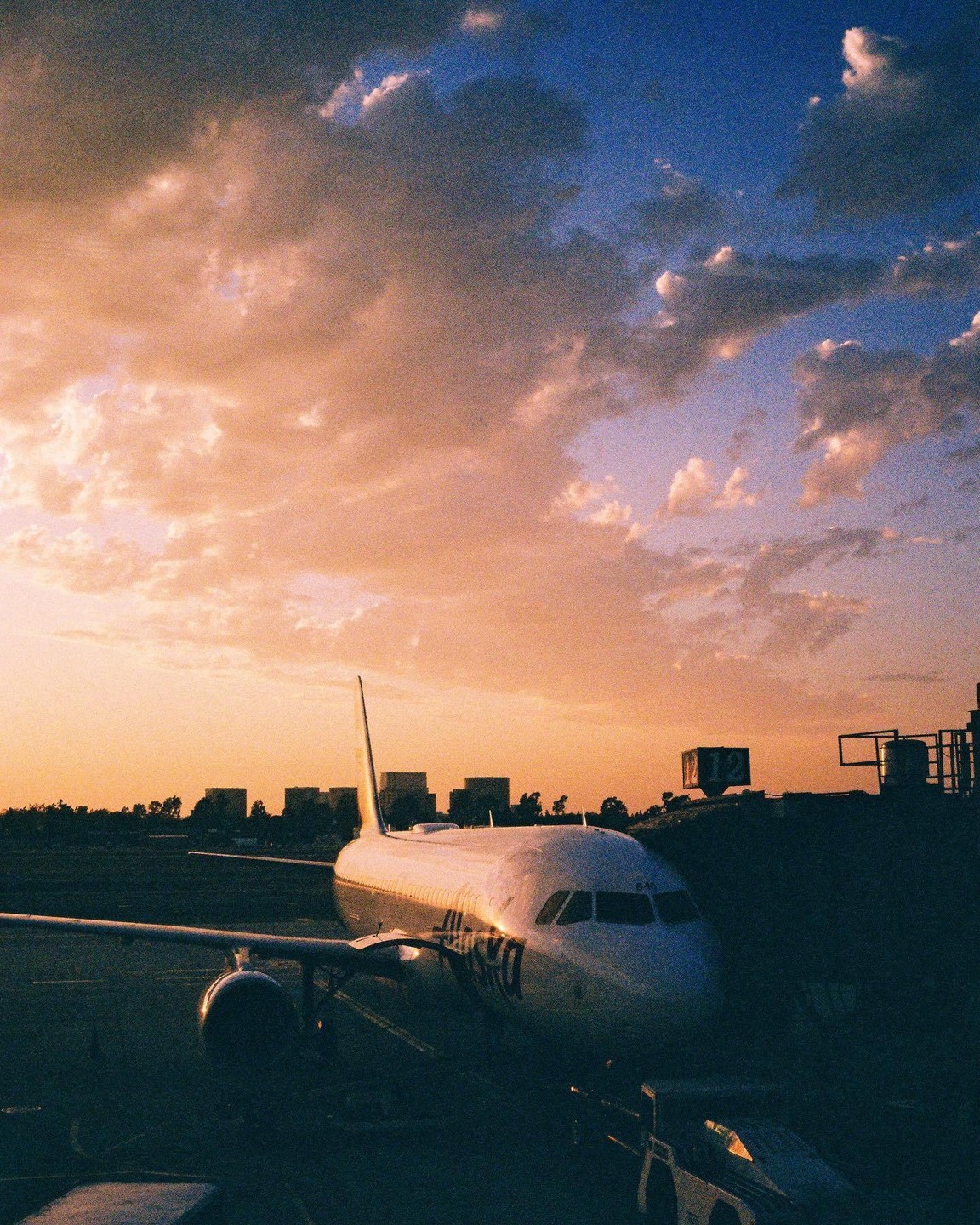 An airplane is parked on the tarmac at sunset with a colorful sky.
