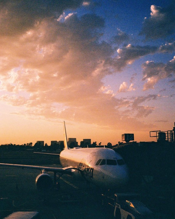 An airplane is parked on the tarmac at sunset with a colorful sky.