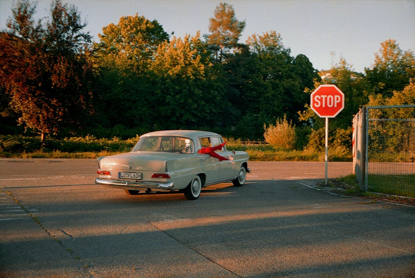 A woman's legs in red tights hang out of the passenger window of a vintage car next to a stop sign.